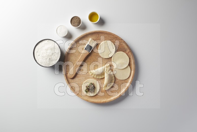 two closed sambosas and one open sambosa filled with meat while flour, salt, black pepper and oil with oil brush aside in a wooden dish on a white background