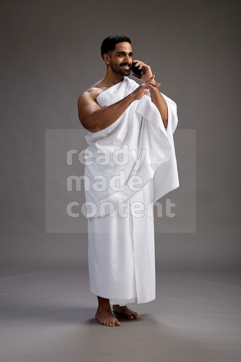 A man wearing Ehram Standing talking on phone on gray background