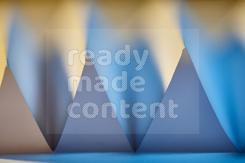 A close-up abstract image showing sharp geometric paper folds in blue gradients and warm tones