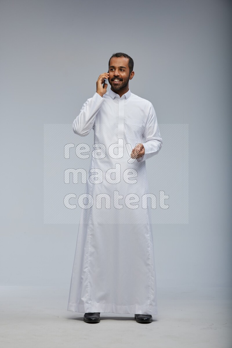 Saudi man wearing Thob standing talking on phone on Gray background