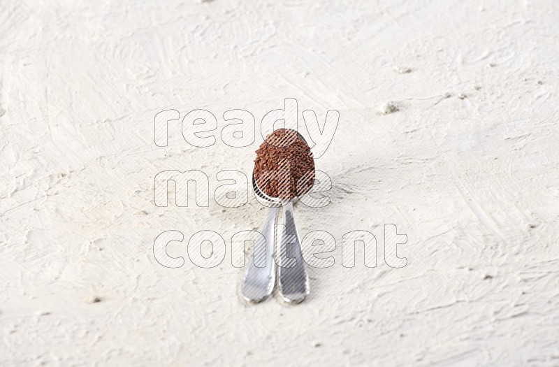 2 metal spoons full of garden cress seeds on a textured white flooring