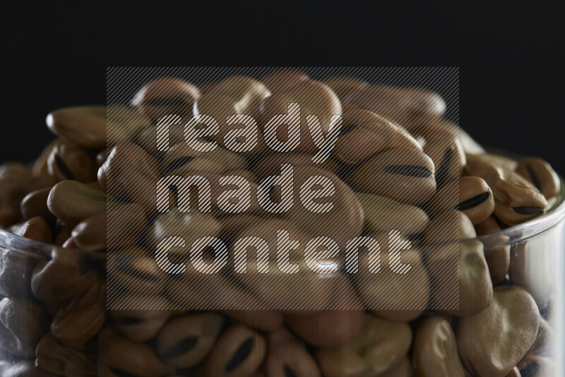 Fava beans in a glass jar on black background