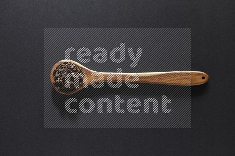A wooden ladle full of whole cloves on a black flooring
