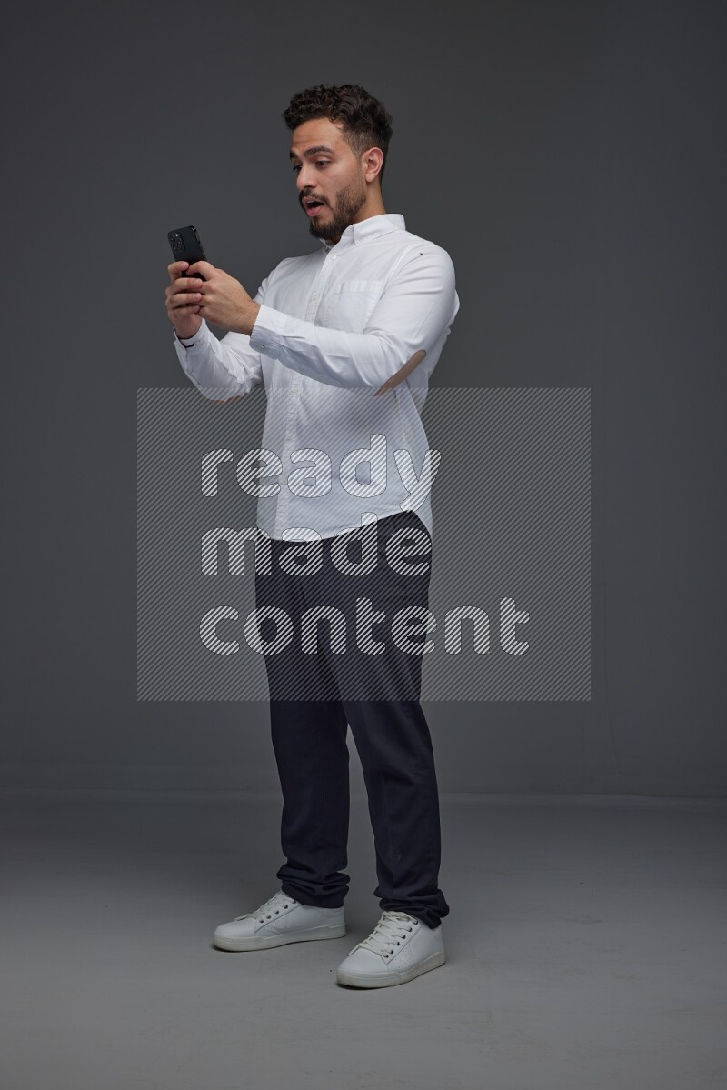 A man wearing smart casual standing and using his phone eye level on a gray background
