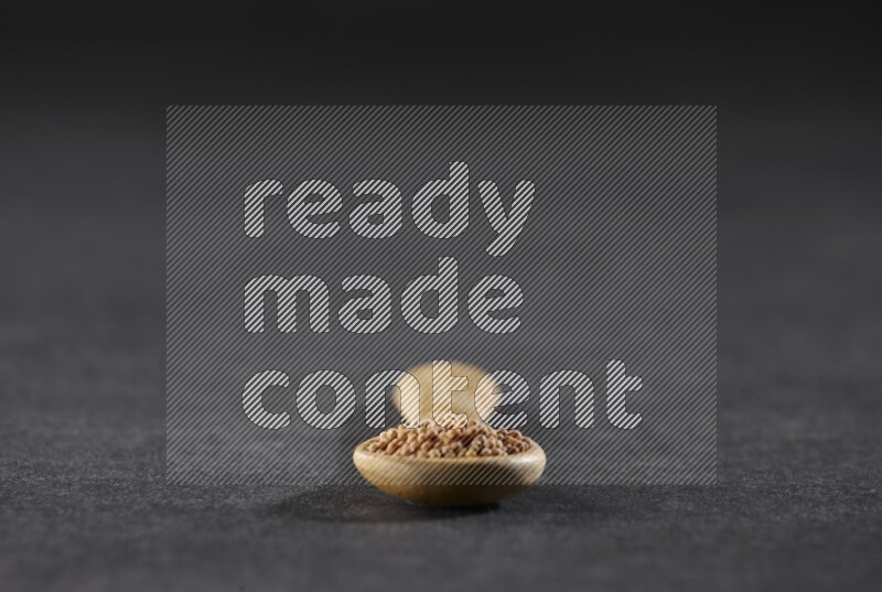 A wooden spoon full of mustard seeds on a black flooring