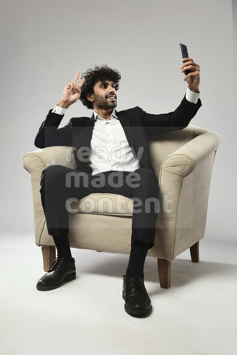 رجل يرتدي ملابس رسمية يجلس علي كرسي و يلتقط صورة شخصية علي خلفية بيضاء