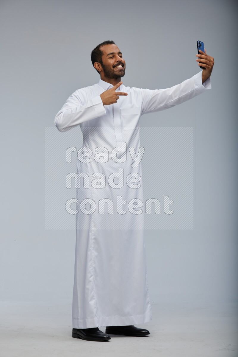 Saudi man wearing Thob standing taking selfie on Gray background