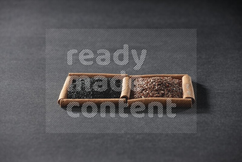 2 squares of cinnamon sticks full of flaxseeds and black seeds on black flooring