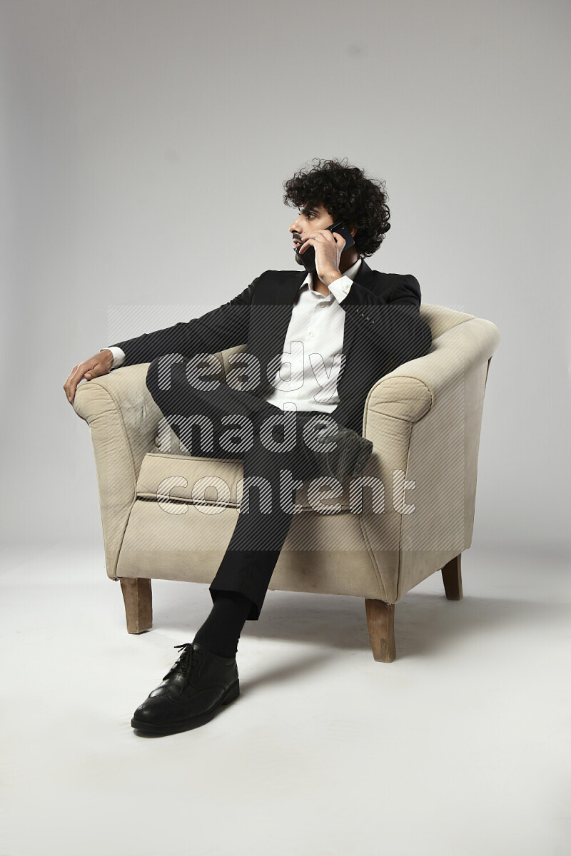 رجل يرتدي ملابس رسمية يجلس علي كرسي و يتحدث في الهاتف علي خلفية بيضاء
