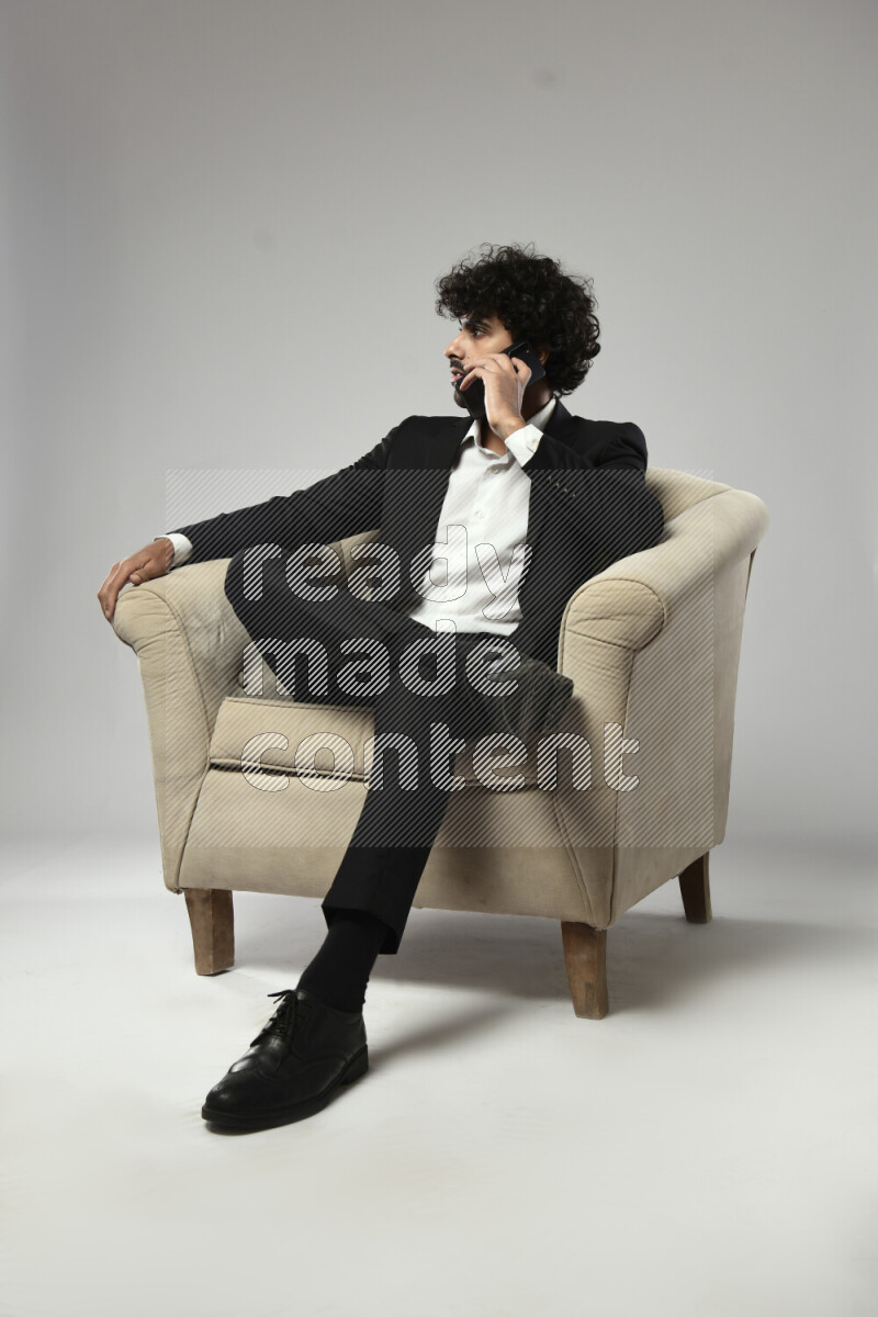 A man wearing formal sitting on a chair talking on the phone on white background
