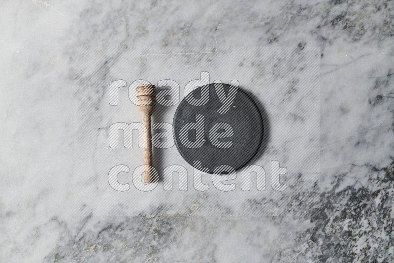 Black Pottery Plate with wooden honey handle on the side on grey marble flooring, Top view