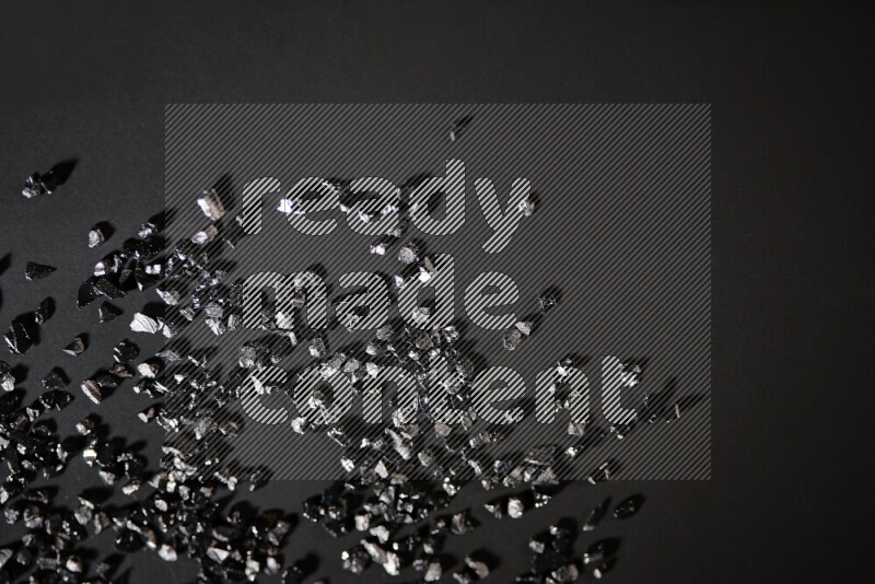 Black shimmering fragments of glass scattered on a black background