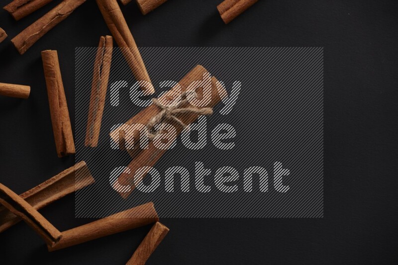 4 Cinnamon sticks stacked and bounded with more sticks in the background on black flooring