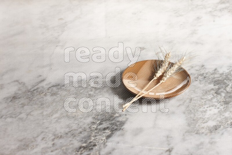 Wheat stalks on multicolored pottery plate on grey marble background