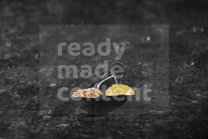 Two metal spoons, one filled with mustard seeds and the other with mustard paste on black background