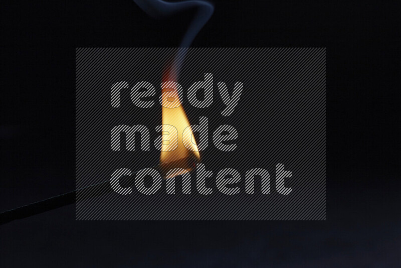A burning incense stick isolated on dark backdrop