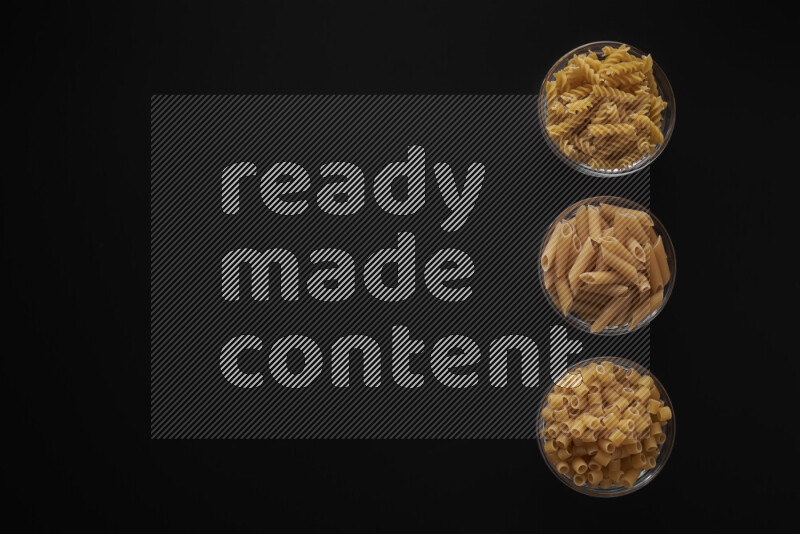 Different pasta types in 3 glass bowls on black background