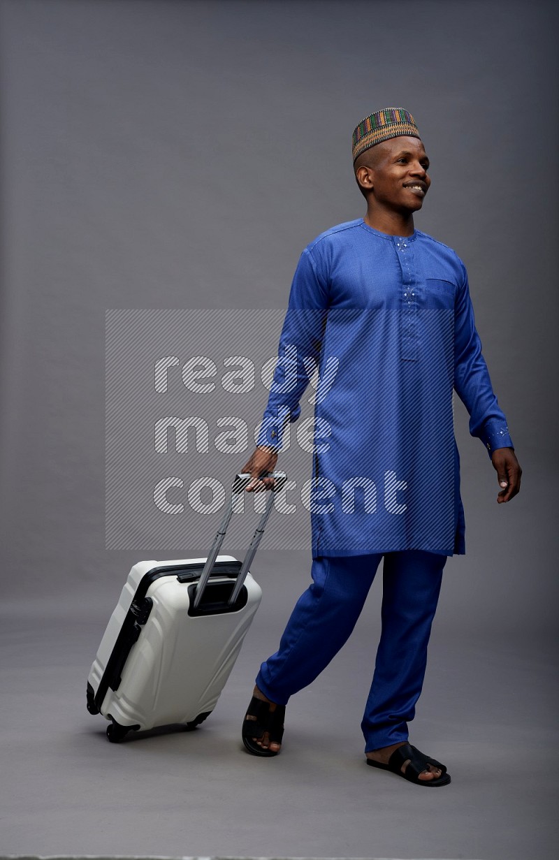 Man wearing Nigerian outfit standing holding bag on gray background