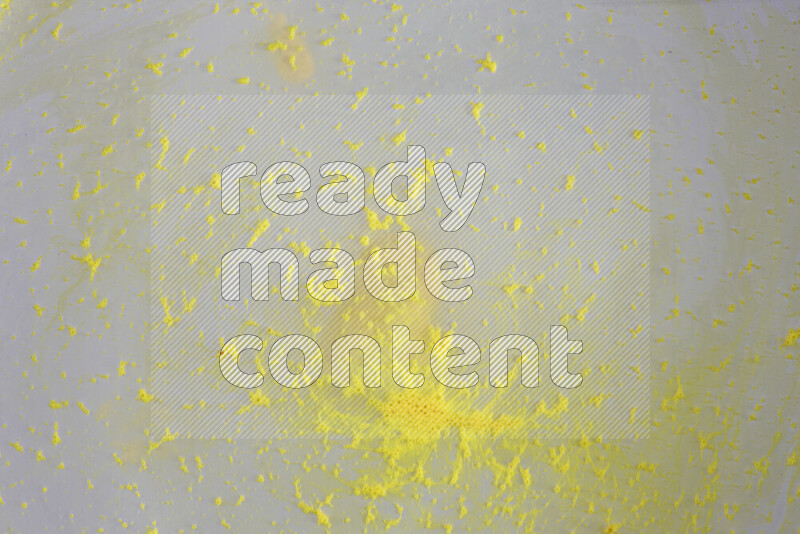 The image captures a dramatic splatter of yellow paint over a white backdrop