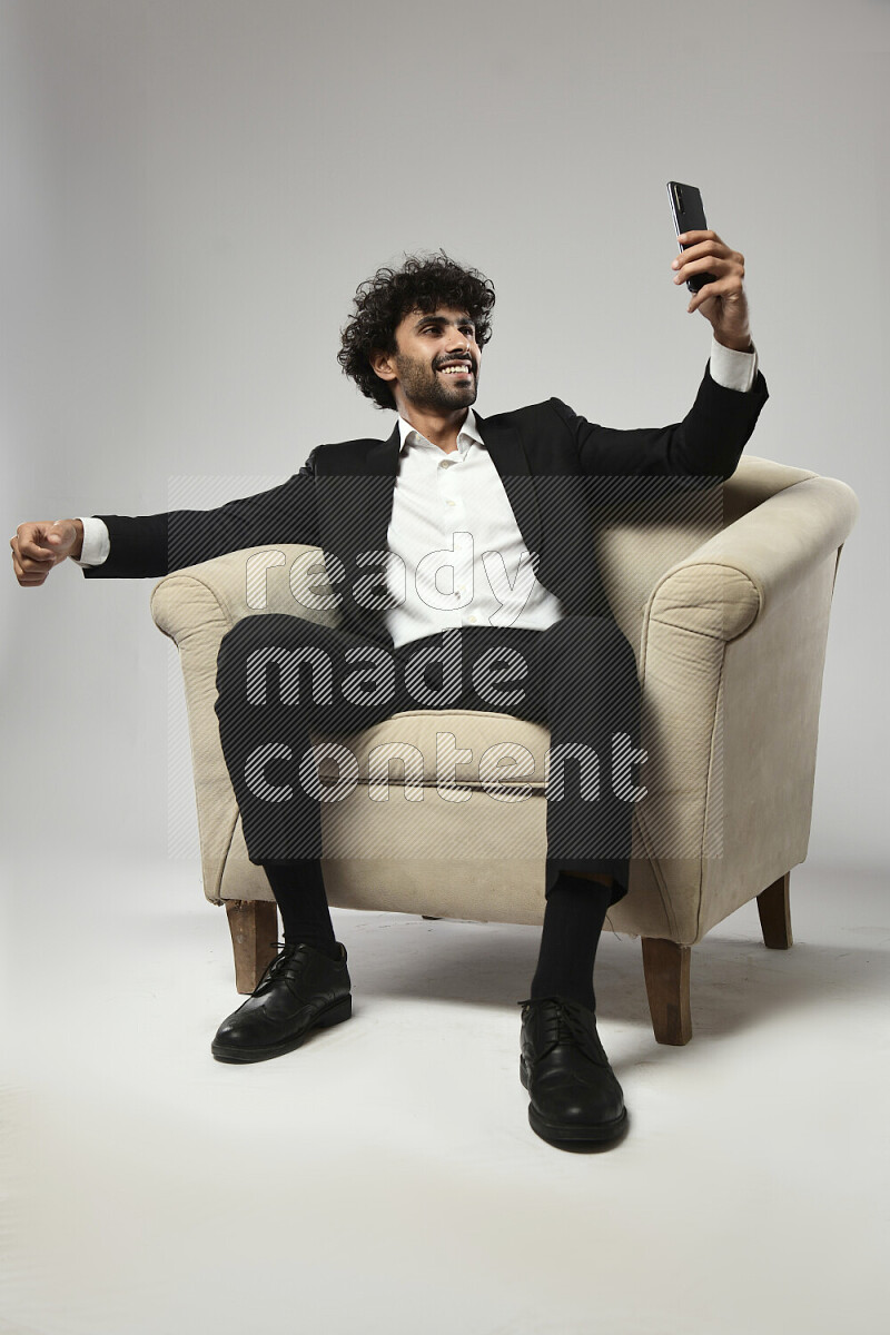 A man wearing formal sitting on a chair taking a selfie on white background