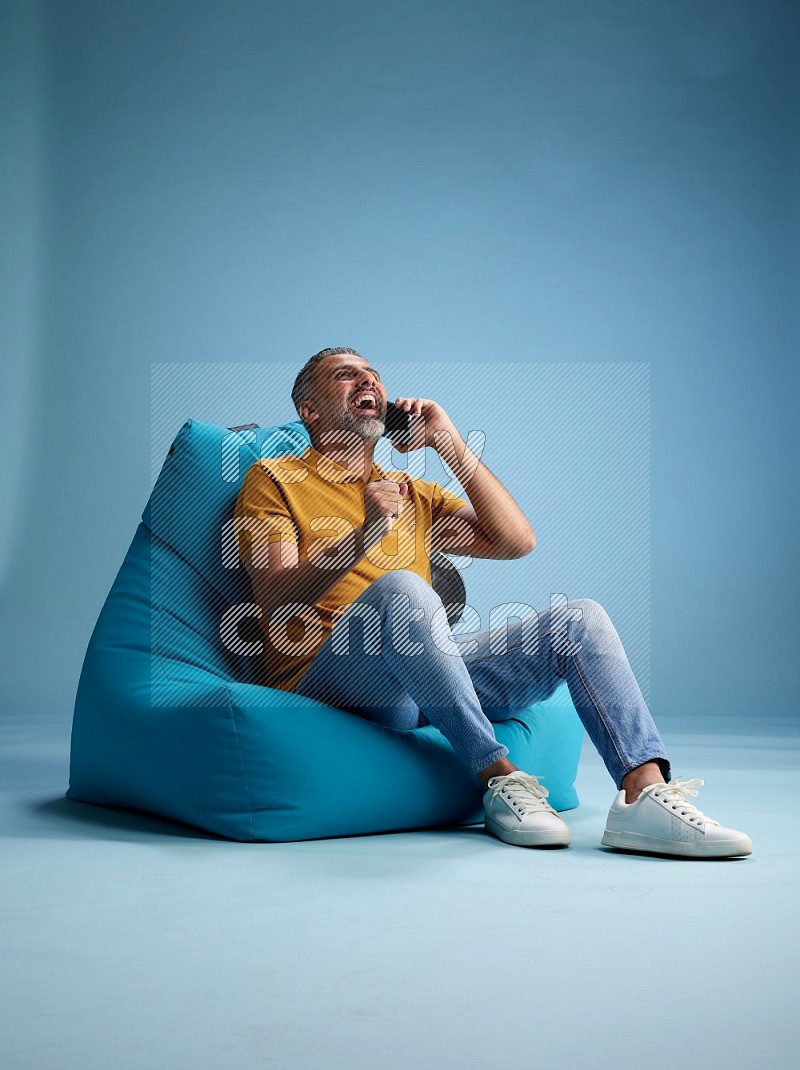 A man sitting on a blue beanbag and talking on the phone