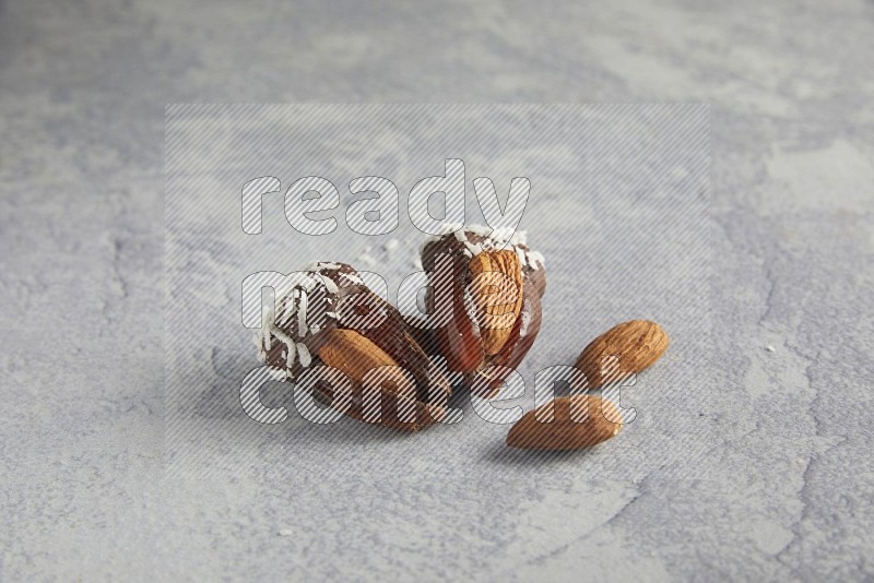 Two Almond stuffed dates covered with dark chocolate and coconut on a light grey background