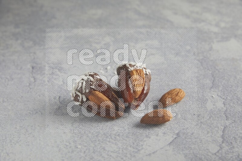 Two Almond stuffed dates covered with dark chocolate and coconut on a light grey background