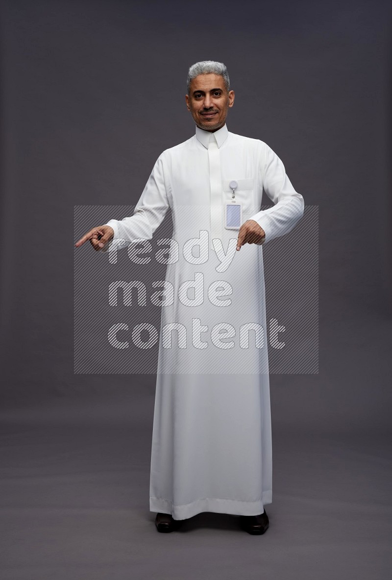 Saudi man wearing thob with pocket employee badge standing interacting with the camera on gray background