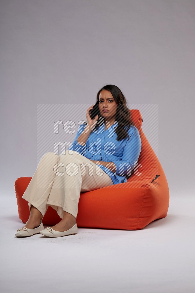 A woman sitting on an orange beanbag and talking on the phone