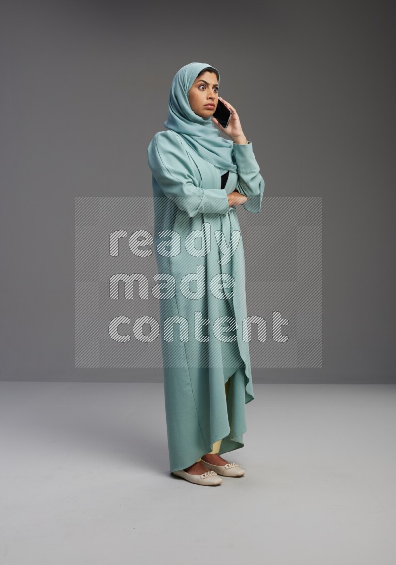 Saudi Woman wearing Abaya standing talking on phone on Gray background