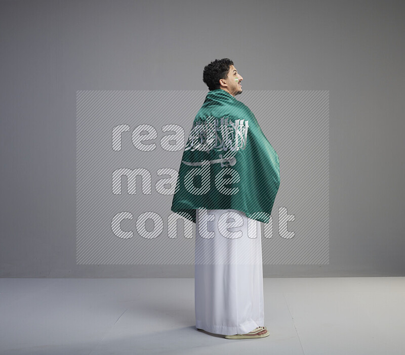 رجل سعودي يرتدي ثوب ابيض يلف علم السعودية حوله