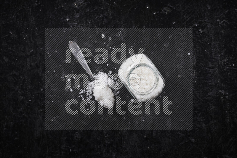 وعاء زجاجي ممتلئ بملح البحر الخشن على خلفية سوداء