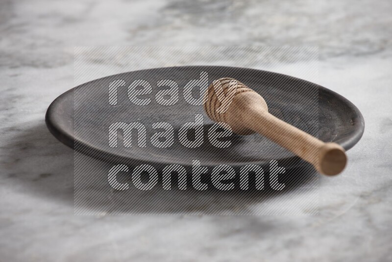 طبق فخاري أسود مع ملعقة عسل خشبية بداخله على خلفية من الرخام الرمادي