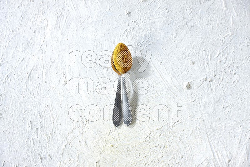 2 metal spoons full of turmeric powder on a textured white background