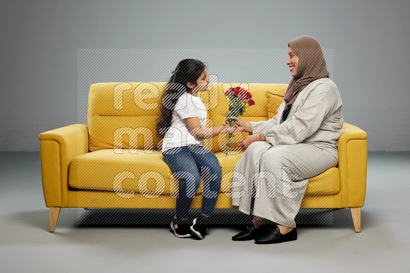 A girl sitting giving flowers to her mother on gray background