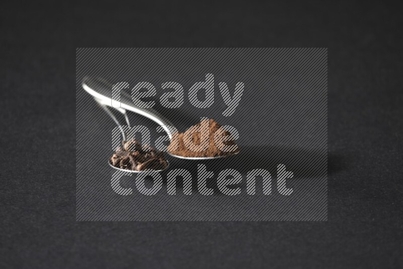 ملعقتان معدنيتان، إحداهما ممتلئة بحبوب القرنفل والأخرى ببودرة القرنفل، على خلفية سوداء