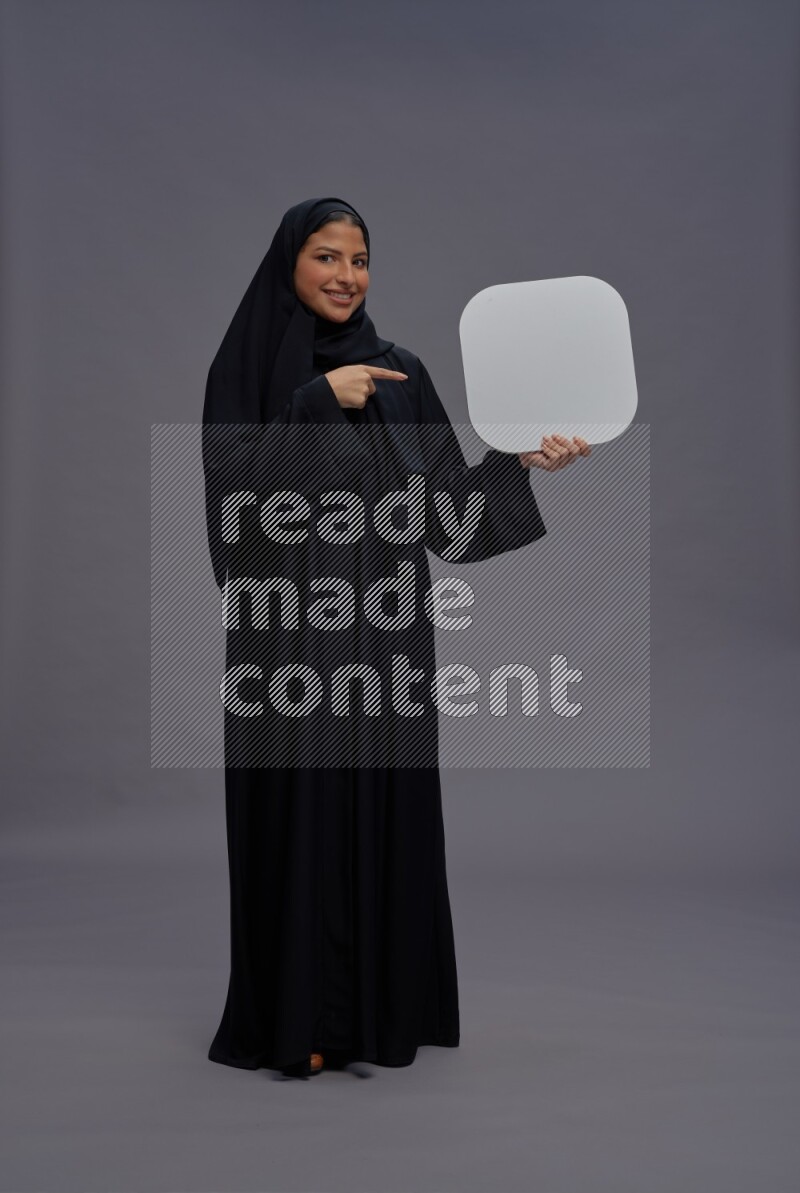 Saudi woman wearing Abaya standing holding social media sign on gray background