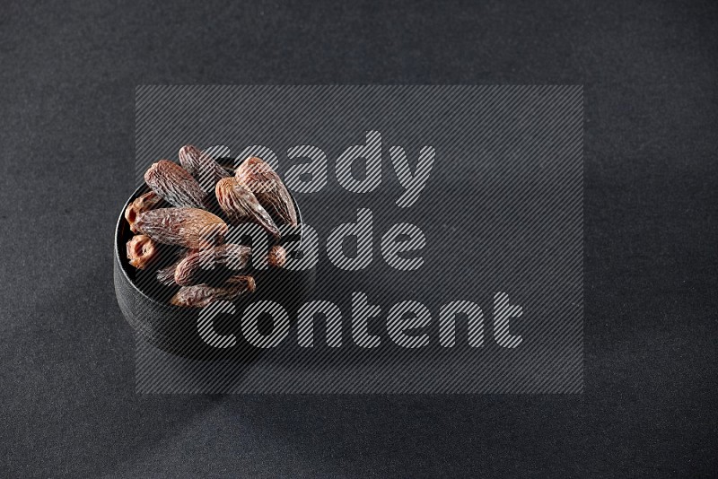 A black pottery bowl full of dried dates on a black background in different angles