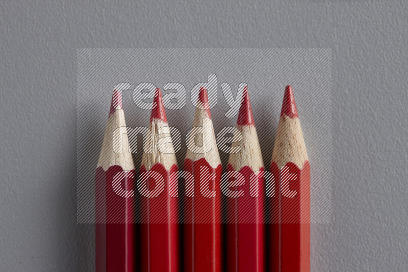 A collection of sharpened colored pencils arranged showcasing a gradient of red hues on grey background