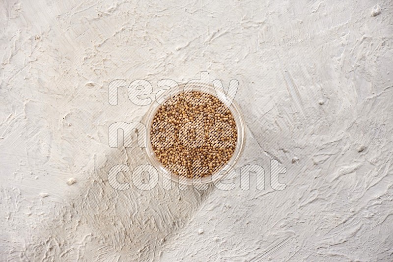 A glass jar full of mustard seeds on a textured white flooring