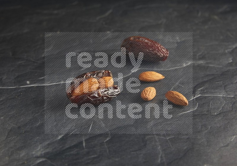 two almond stuffed madjoul dates on a black textured background