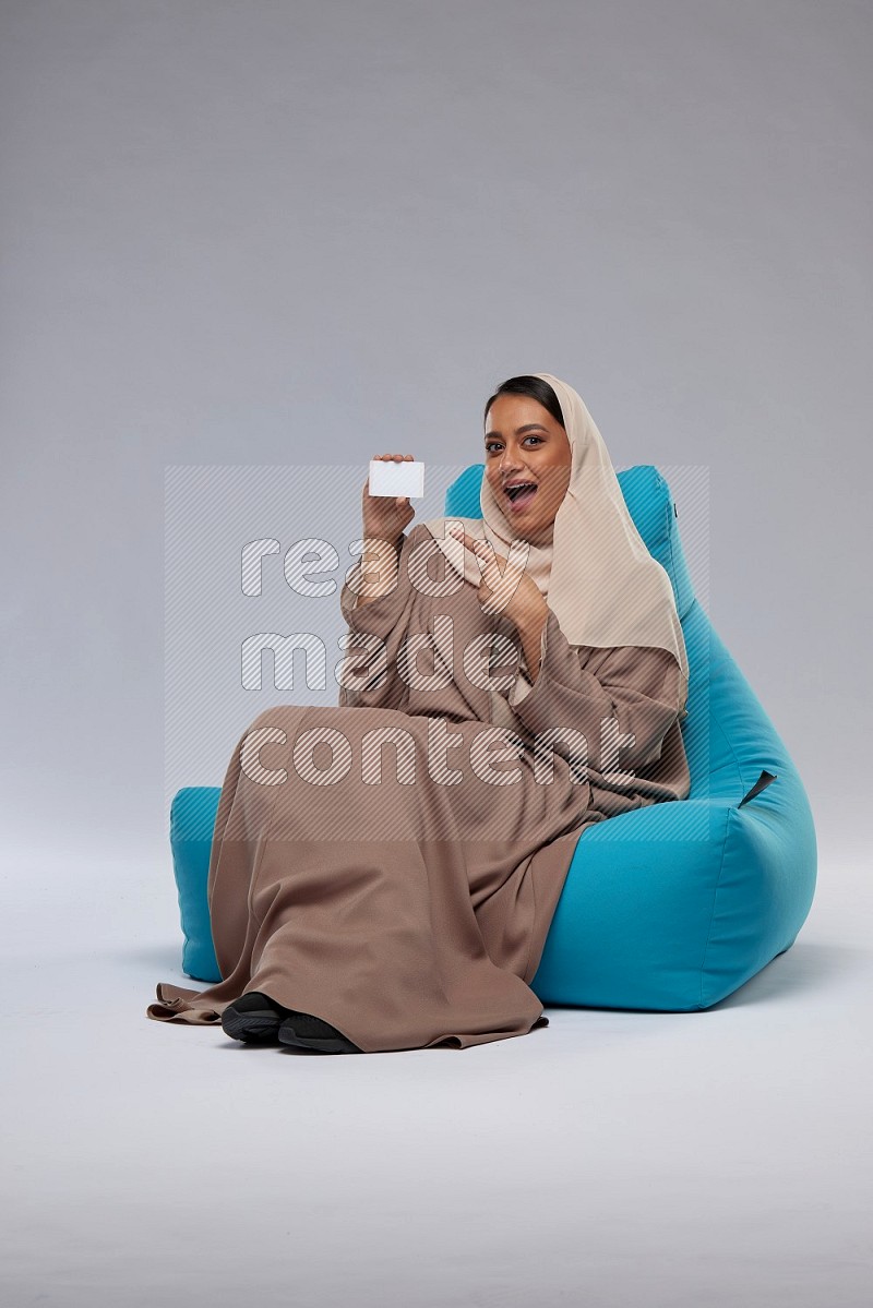 A Saudi woman sitting on a blue beanbag and holding ATM card