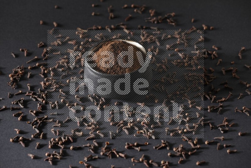 وعاء فخاري أسود ممتلئ ببودرة القرنفل وحبوب القرنفل على خلفية سوداء