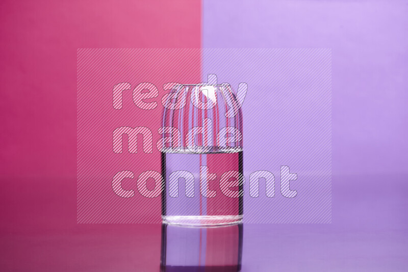 The image features a clear glassware filled with water, set against pink and light purple background