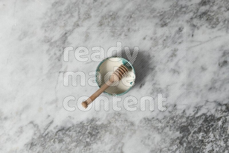Multicolored pottery bowl with wooden honey dipper in it on grey marble background
