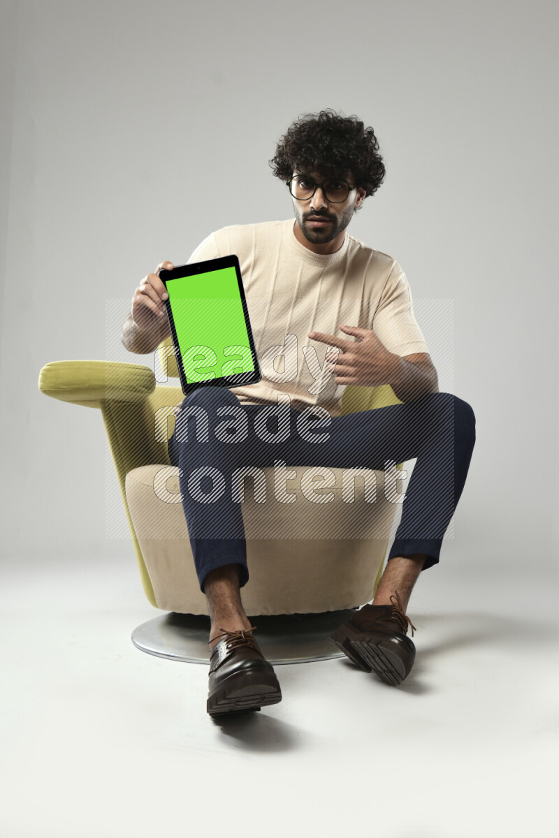 A man wearing casual sitting on a chair showing a tablet screen on white background