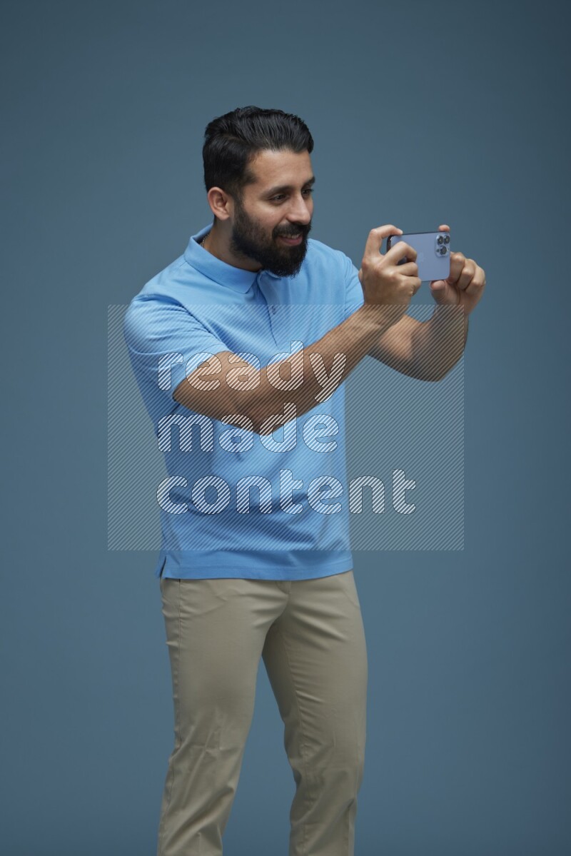 Man taking a picture with his phone  in a blue background wearing a Blue shirt