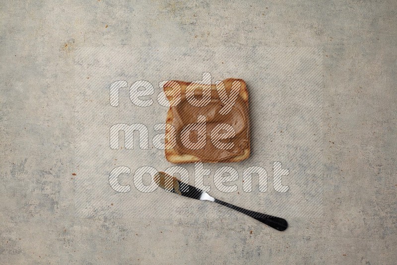 Creamy peanut butter on a toasted white toast slices with a spreading knife on a light blue textured background