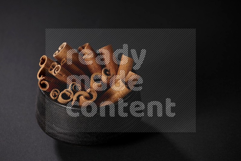 Cinnamon sticks in a black bowl on a black background in different angles