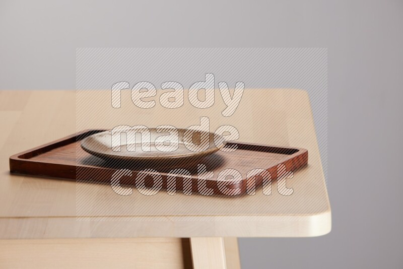 multi-colored pottery Plate placed on a rectangular wooden tray on the edge of wooden table